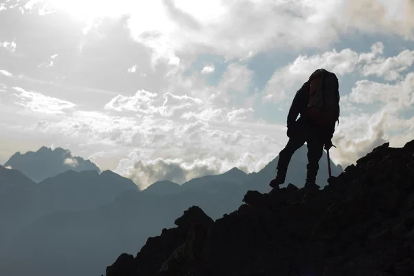 Hiker on top, silhouetted in high mountains