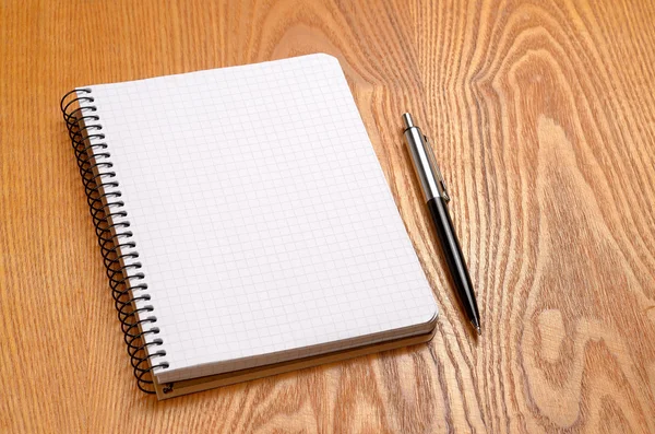 A white note book with black pen on wooden table