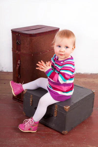 Small baby girl sitting on the old wooden box with a suitcase