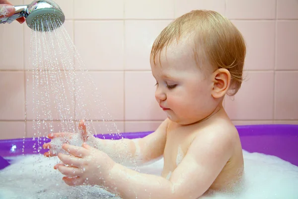 Small baby girl washes in a baby bath with water spray