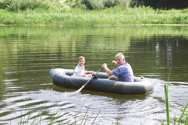 Grandfather with grandson swim in a rubber boat on the river.