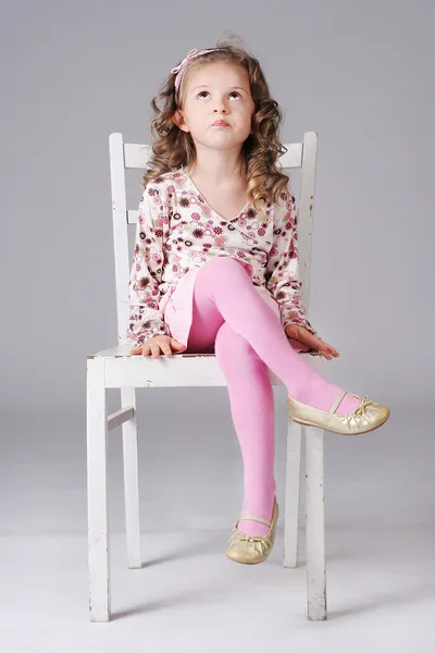 Sweet little girl sitting on the white chair, looking away, maki