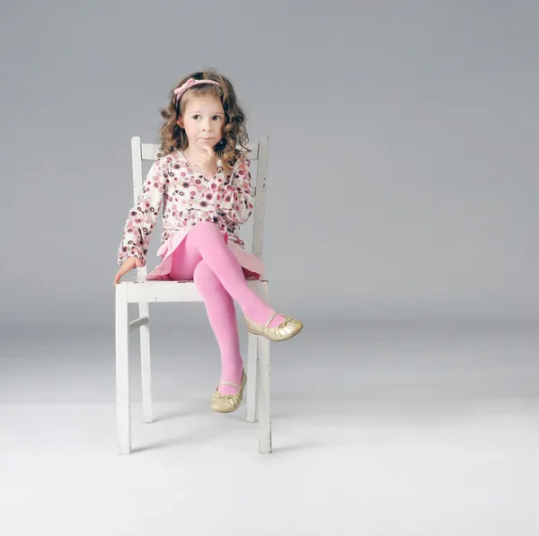 Sweet thoughtful little girl sitting on the white chair, a lot o