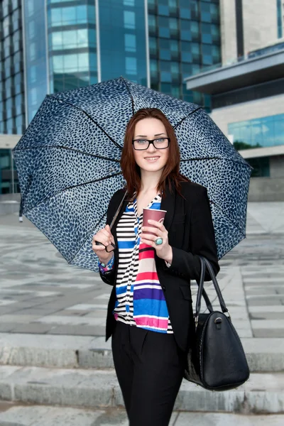 Secretary under an umbrella with a coffee and a bag on the building background