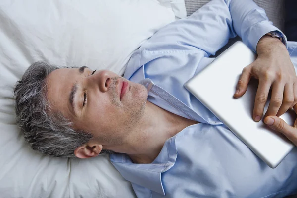 Man sleeping on bed with holding a digital tablet