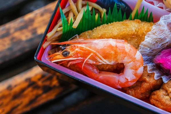 Japanese meal (Bento) in paper boxes on a wood bench