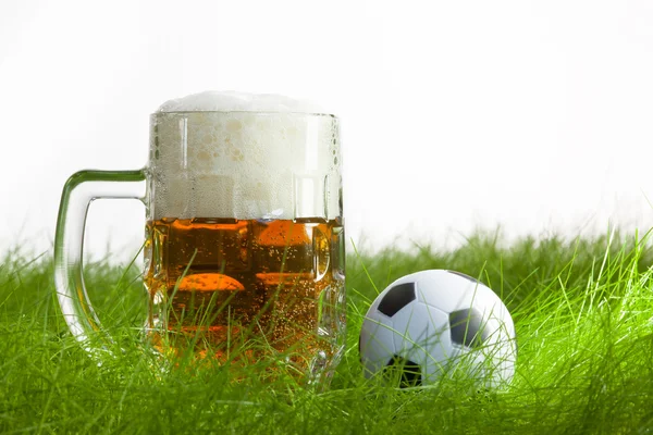 Mug of beer and soccer ball on grass