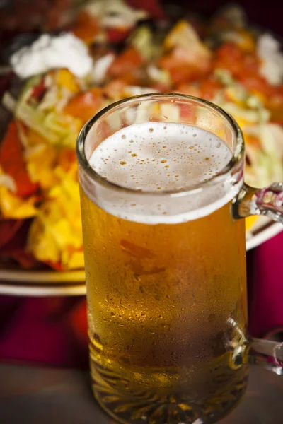 Food and Drink. A closeup image of a cold, frosty mug of beer with a plate of spicy nachos