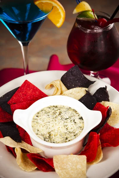 Food and Drink. An appetizer of cheesy spinach and artichoke dip with tortilla chips and cocktails.