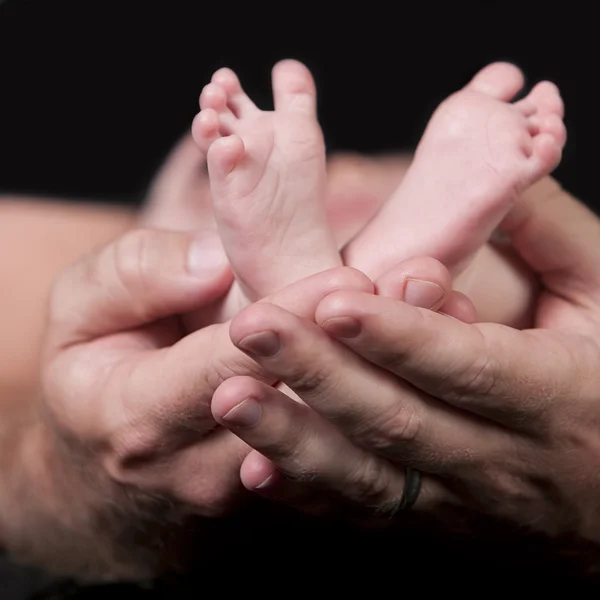 Real. Father hands holding his newborn sons tiny little feet