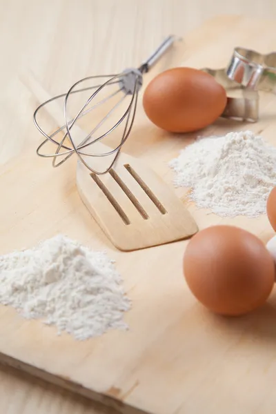 Eggs, flour, cookie mold and whisk on wooden board