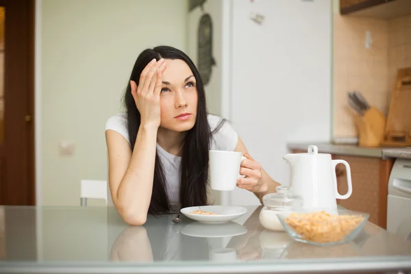 Girl having breakfast in the kitchen with headache