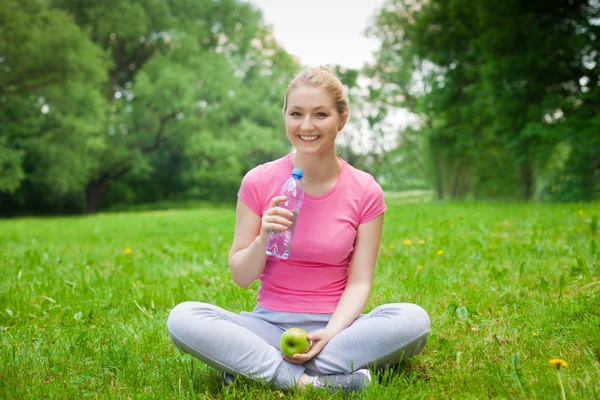 Blonde girl outdoor in the park with water and apple