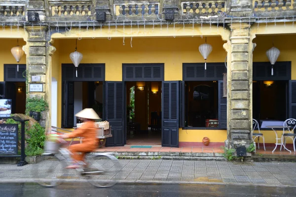 Local Cyclist in non la traditional hat against French colonial architecture in Hoi An, Vietnam