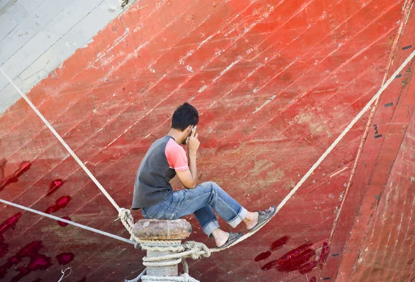 Asian man on the phone in front of the bow of a schooner
