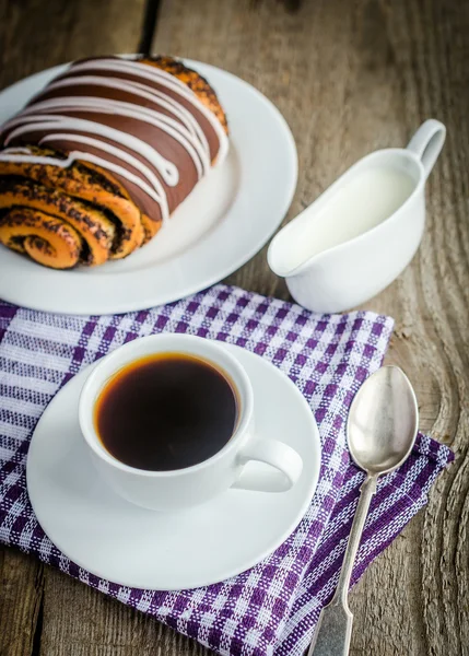 Cup of coffee and poppy bun glazed with ganache