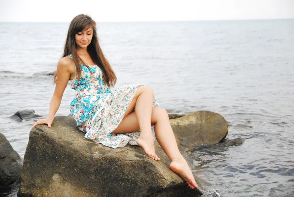 Young girl with long dark hair posing on the huge rocks by the sea