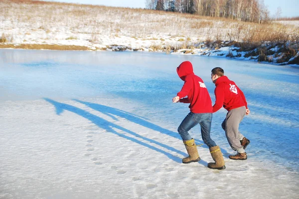 Young guys run across the ice on a frozen lake on a sunny winter day