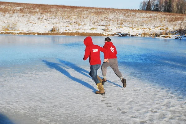 Young guys run across the ice on a frozen lake on a sunny winter day