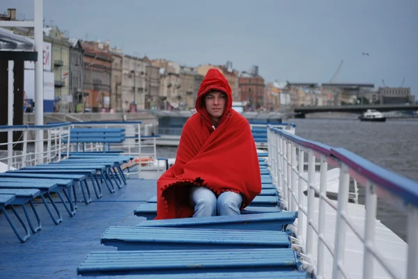 Young man basks under a blanket while riding on a boat on the Neva River in St. Petersburg