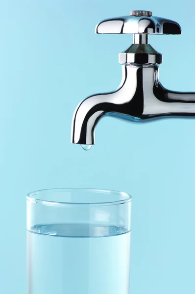 Glass of water and tap with drop.