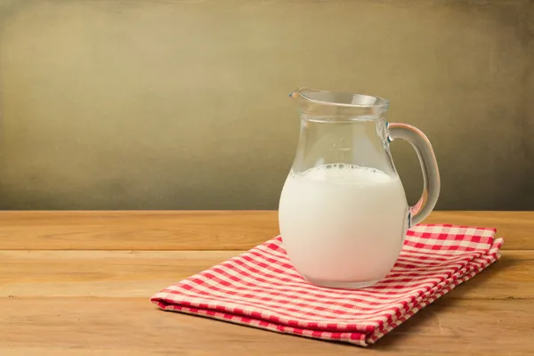 Milk pitcher on tablecloth over grunge background