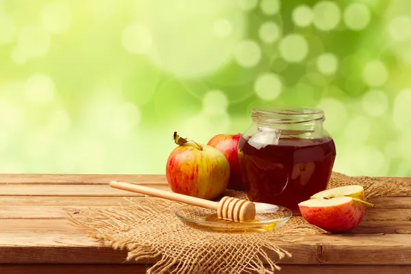 Honey and apples on wooden table over bokeh garden background