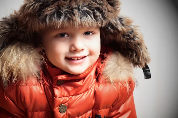 Smiling child in fur hood and orange winter jacket. fashionable boy