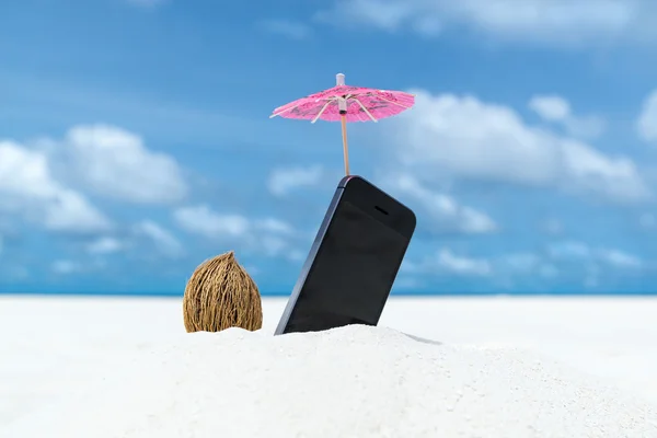 Mobile phone and cocktail umbrella on the beach with the sea in the background