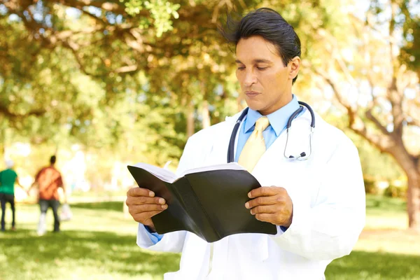 Hispanic Doctor Reading The Bible In The Park