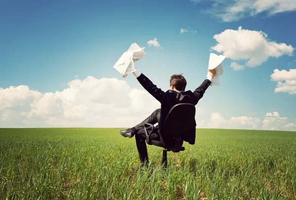 Businessman sitting on a chair in a field and holding documents