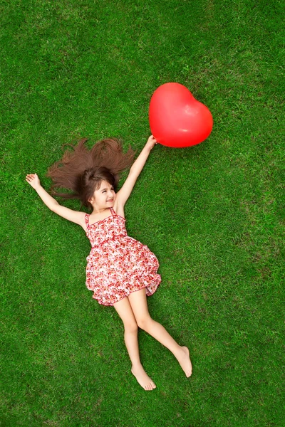 Beautiful girl lying on the grass and holding a red ball in the