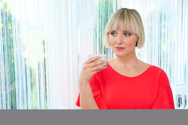 Woman with coffee looking through window