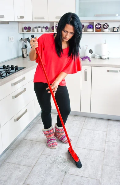 Attractive woman cleaning broken glass in kitchen