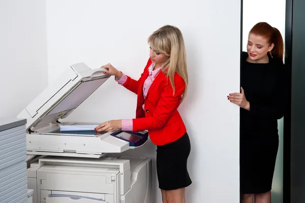 Two woman colleagues working on printer in office