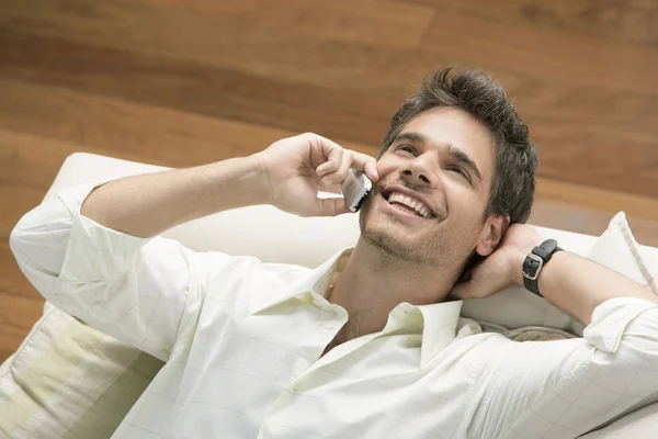 Young professional man using a cell phone while laying down on a sofa.