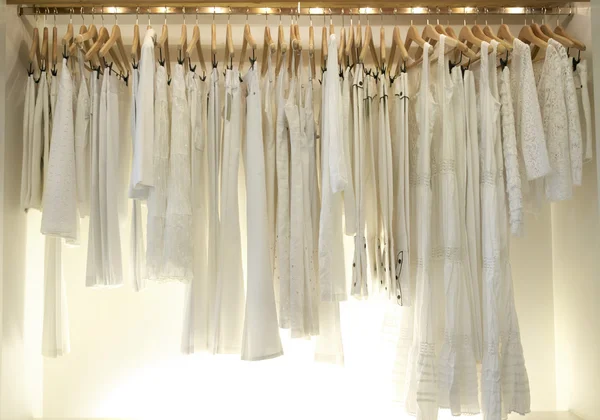 Line of new white clothes hanging on wooden hangers in a fashion store.