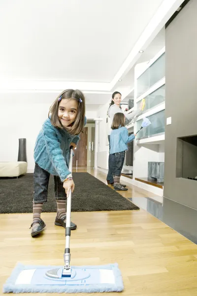 Twin daughters and mum cleaning their home\'s living room.