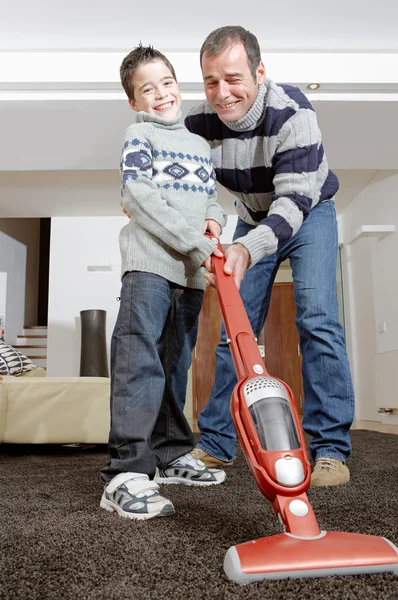 Dad and son vaccum cleaning their living room, smiling and bonding.