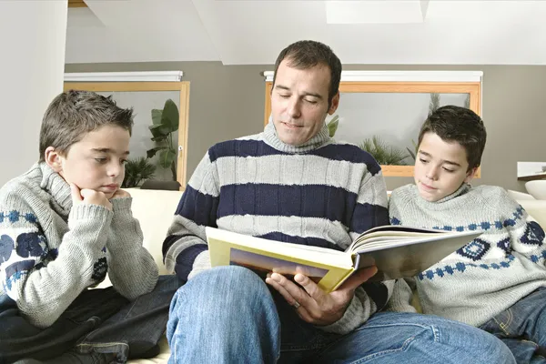 Dad and identical twin sons reading a book at home together.
