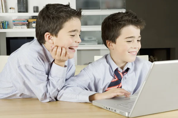 Two twin brothers sharing a laptop computer at home, laughing.