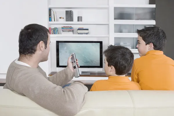 Father with twin brothers watching tv at home, using the control remote.
