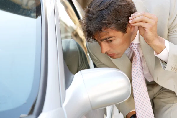 Attractive young businessman grooming using a car's reversing mirror to tidy his hair up.