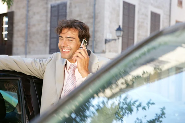 Businessman using a cell phone to make a phone call while standing some cars in the city.