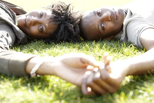 Close up portrait of a young african american couple laying down on green grass in the city