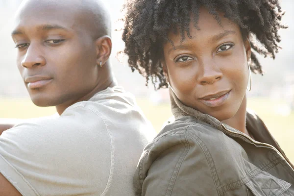 Young attractive african american couple sitting back to back in a city park while on vacation