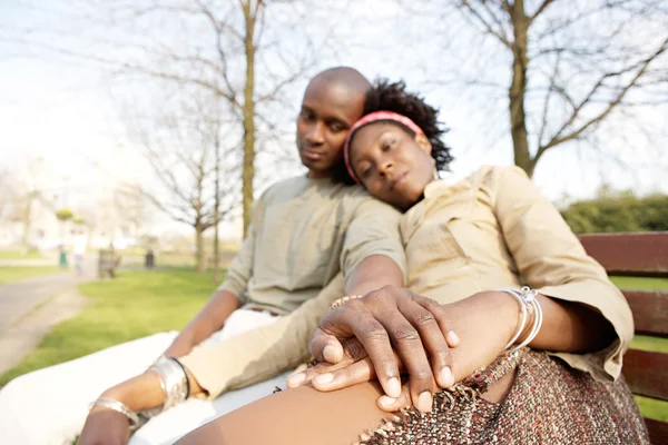 Young attractive black couple sitting down on a bench in the park