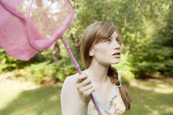 Teenage girl holding a butterfly net in the forest.