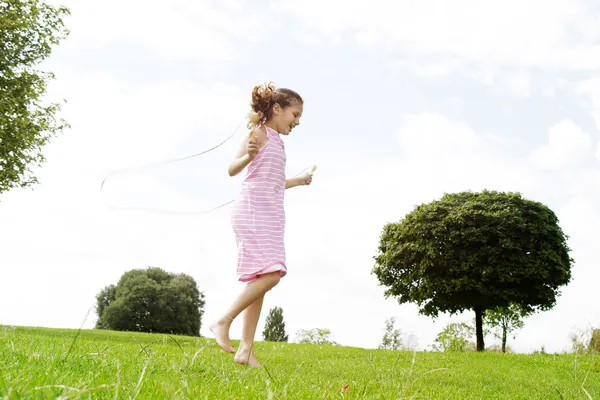 Profile view of a young girl playing skipping rope in the park, smiling.