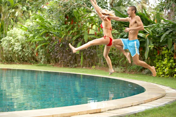 Young fun couple jumping into a tropical swimming pool
